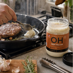 Steak searing in a cast iron skillet with the tallow jar beside the pan