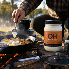 Campfire skillet cooking eggs and potatoes with the tallow jar in frame